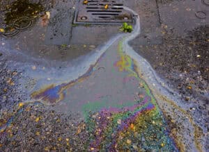 Oil sheen on wet paving running into a road gully, the run-off an oil separator is fitted to intercept.