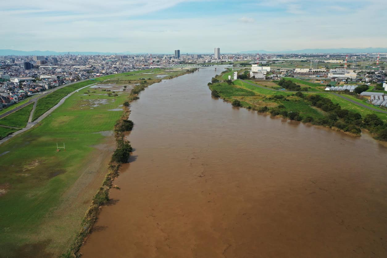 Japanese river in flood, water spread across the floodplain inside the levees as an open levee is designed to allow.