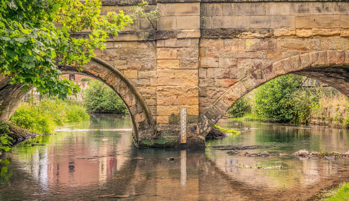 River gauge board on a stone bridge pier, reading water level from a local zero rather than a height above Ordnance Datum.