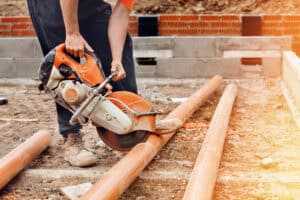 Contractor cutting orange PVC-U pipe on a housing site, where sewers for adoption are built to a fixed specification.