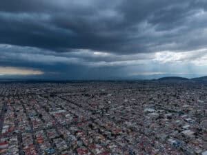 Rain falling over dense low-rise housing on the flat floor of the basin, the ground at the centre of the Mexico City sinking.