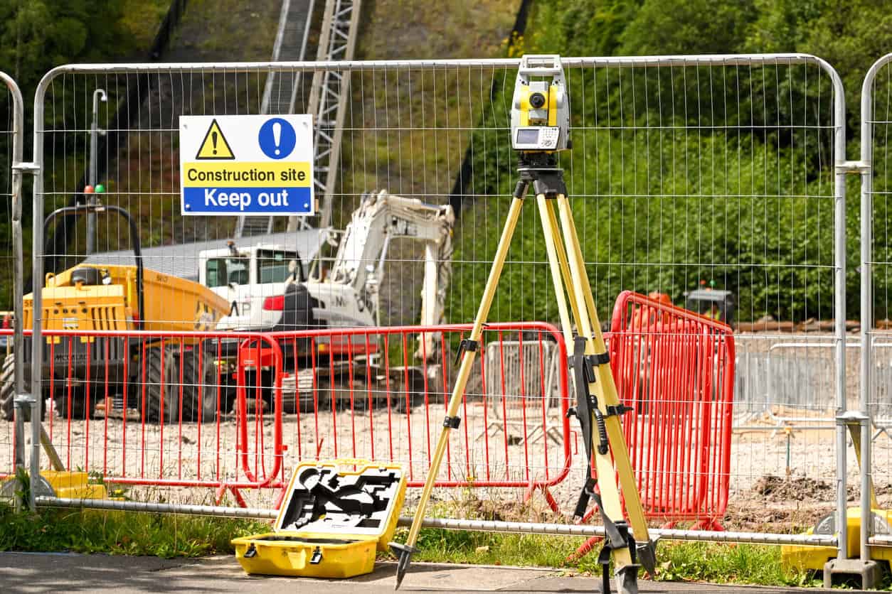 Construction site with surveying equipment and safety barriers in place.