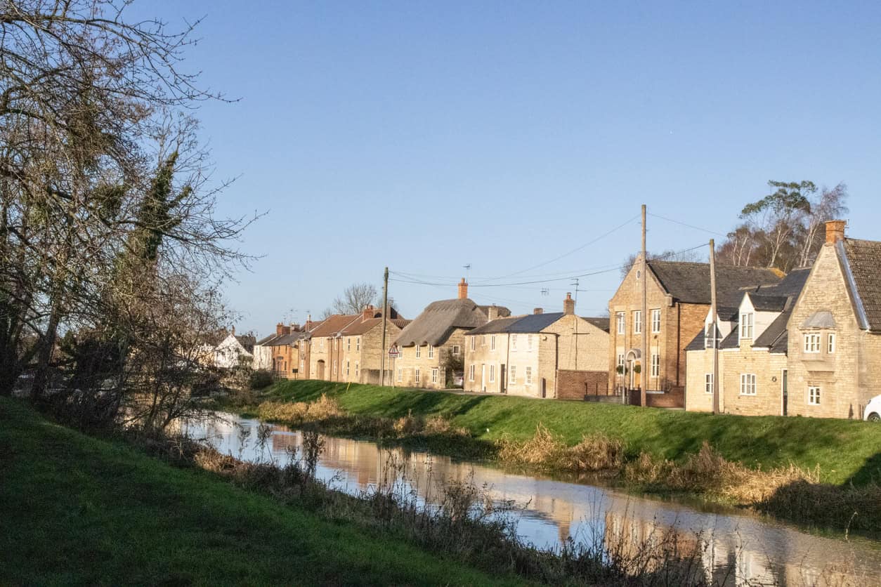 Brick and stone houses beside a straight drainage channel in low-lying pumped farmland.