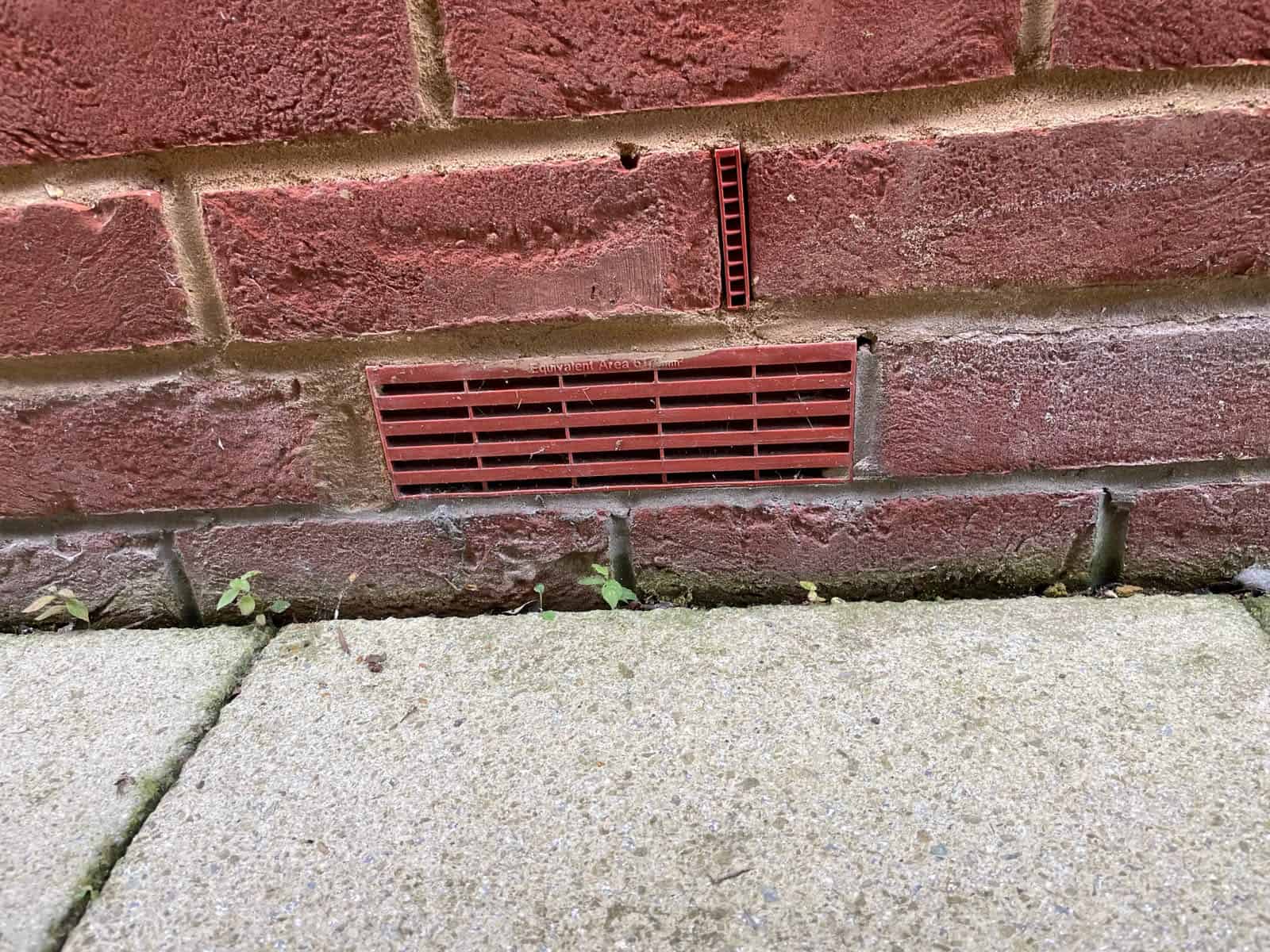 Plastic airbrick and weep vent set low in a brick wall above paving, two entry points that flood defences for homes must seal.