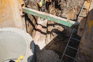 Clay sewer pipe on gravel bedding in a shored trench beside a concrete manhole ring, the kind of pipe a build over agreement protects.