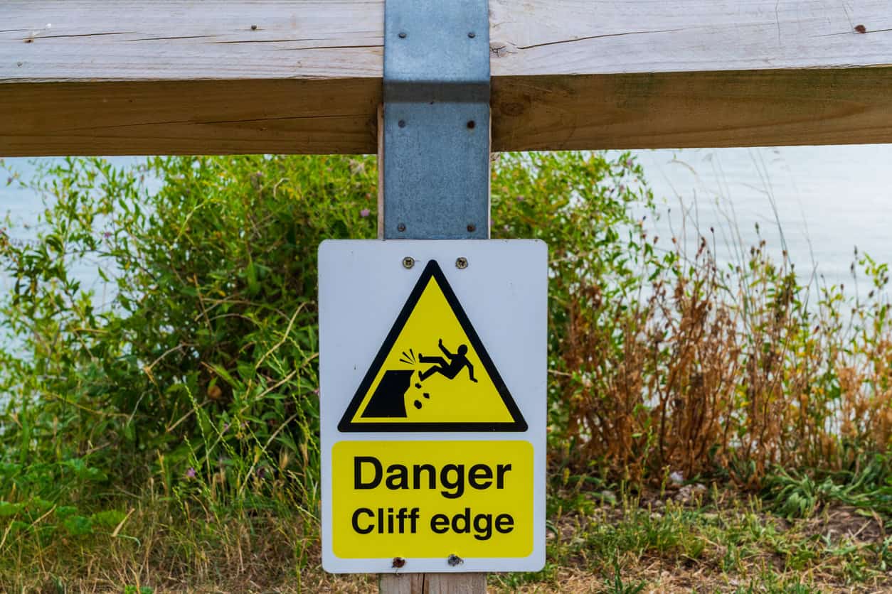 Danger cliff edge sign on a clifftop fence, a common sight where coastal erosion keeps moving the cliff edge inland.