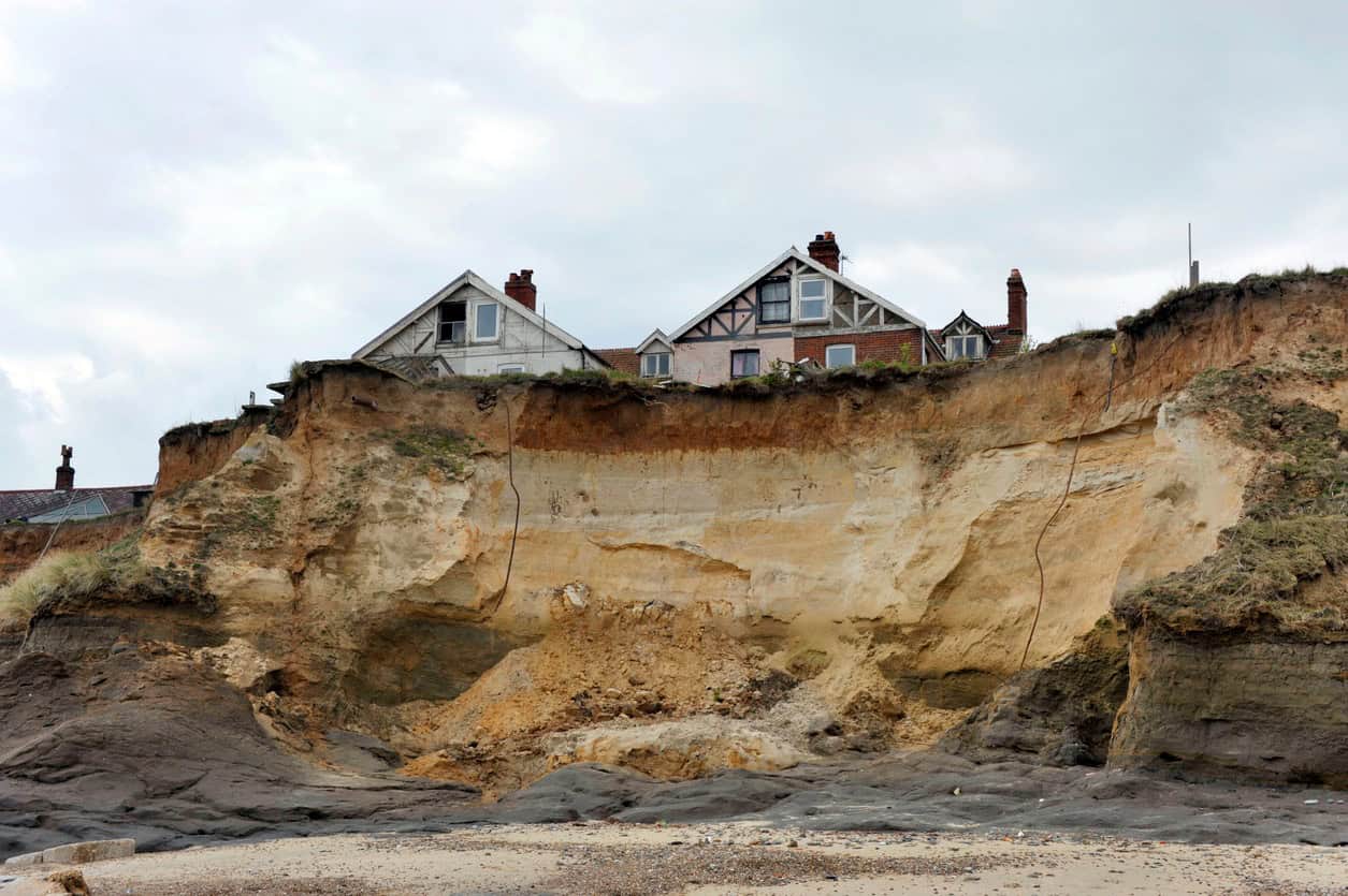 Houses on the edge of a collapsing sand and clay cliff at Happisburgh, Norfolk, after years of coastal erosion.