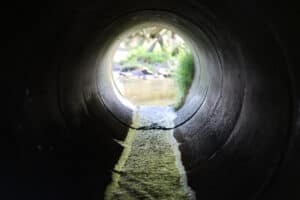View through a concrete pipe culvert barrel towards its outlet and the stream beyond, showing what is a culvert from inside.