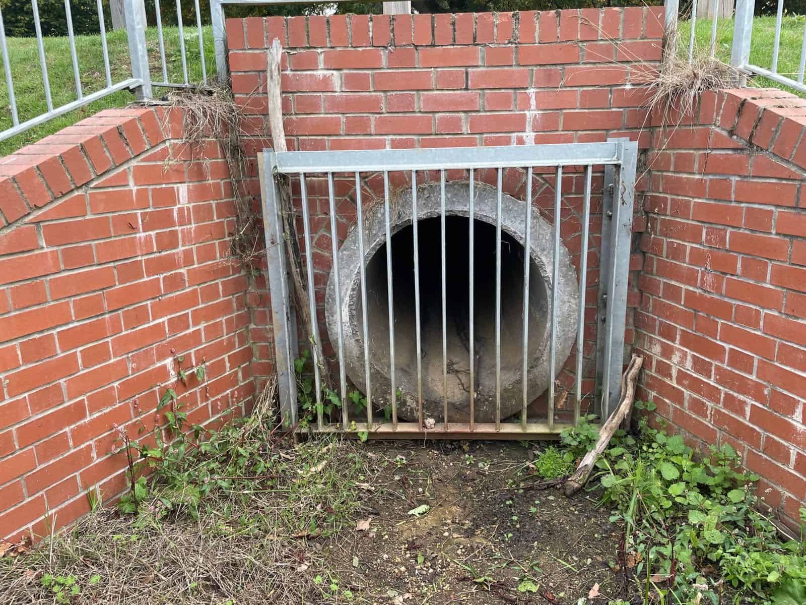 Steel bar screen over a concrete pipe culvert set in a brick headwall with wingwalls, showing what is a culvert inlet.