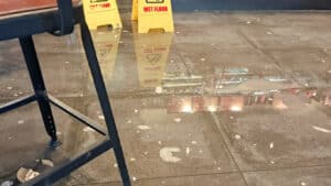 Water pooled across an indoor tiled floor behind wet floor signs, the kind of damage an escape of water claim covers.