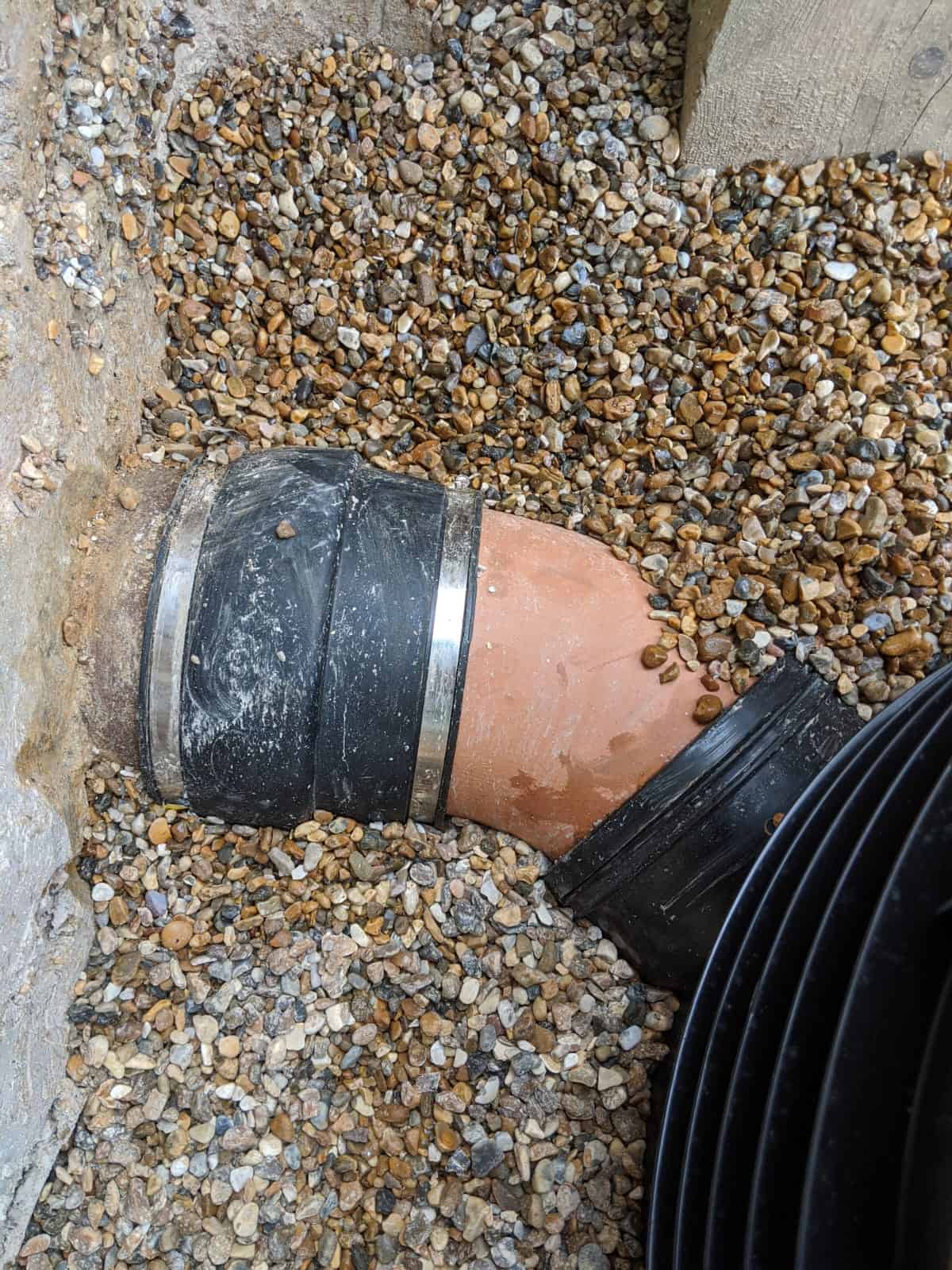 Existing pipe connected through a flexible coupling and clay bend to a new plastic chamber, sewer work a build over agreement can require.