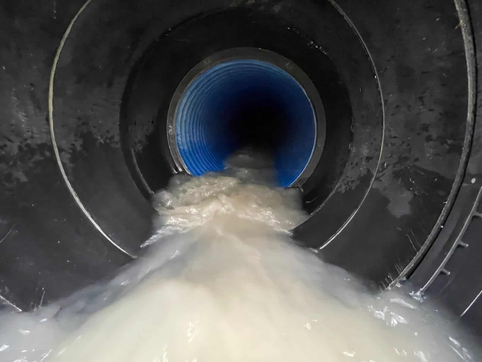 View along a plastic pipe culvert barrel with fast, turbulent flow, illustrating what is a culvert from the inside.