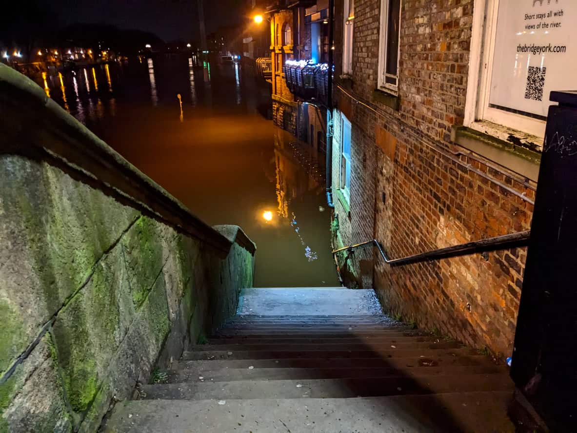 River Ouse floodwater covering the steps beside Ouse Bridge in York at night, with street lights reflected in the water.