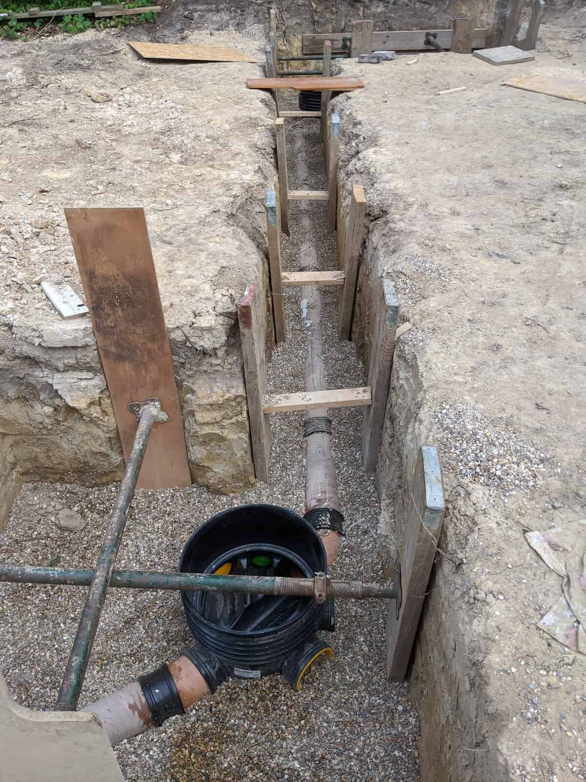 View along a shored sewer trench from a plastic inspection chamber, with the pipe run heading away, typical of build over agreement works.