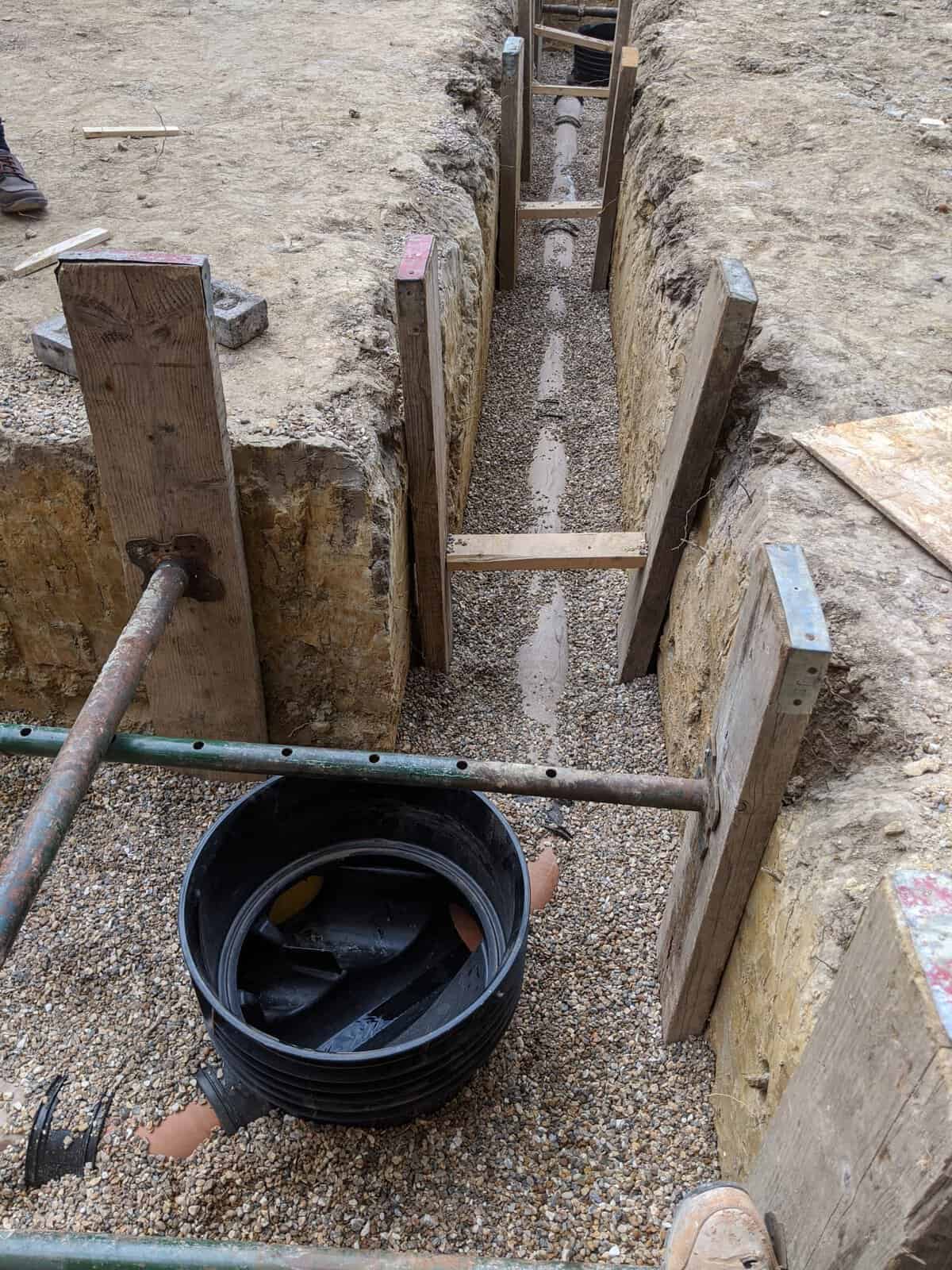 Long timber-shored trench carrying a new sewer pipe run on pea gravel, sewer work of the kind a build over agreement can require.