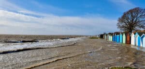 Storm surge floodwater washing past a row of beach huts on a low-lying stretch of coast.