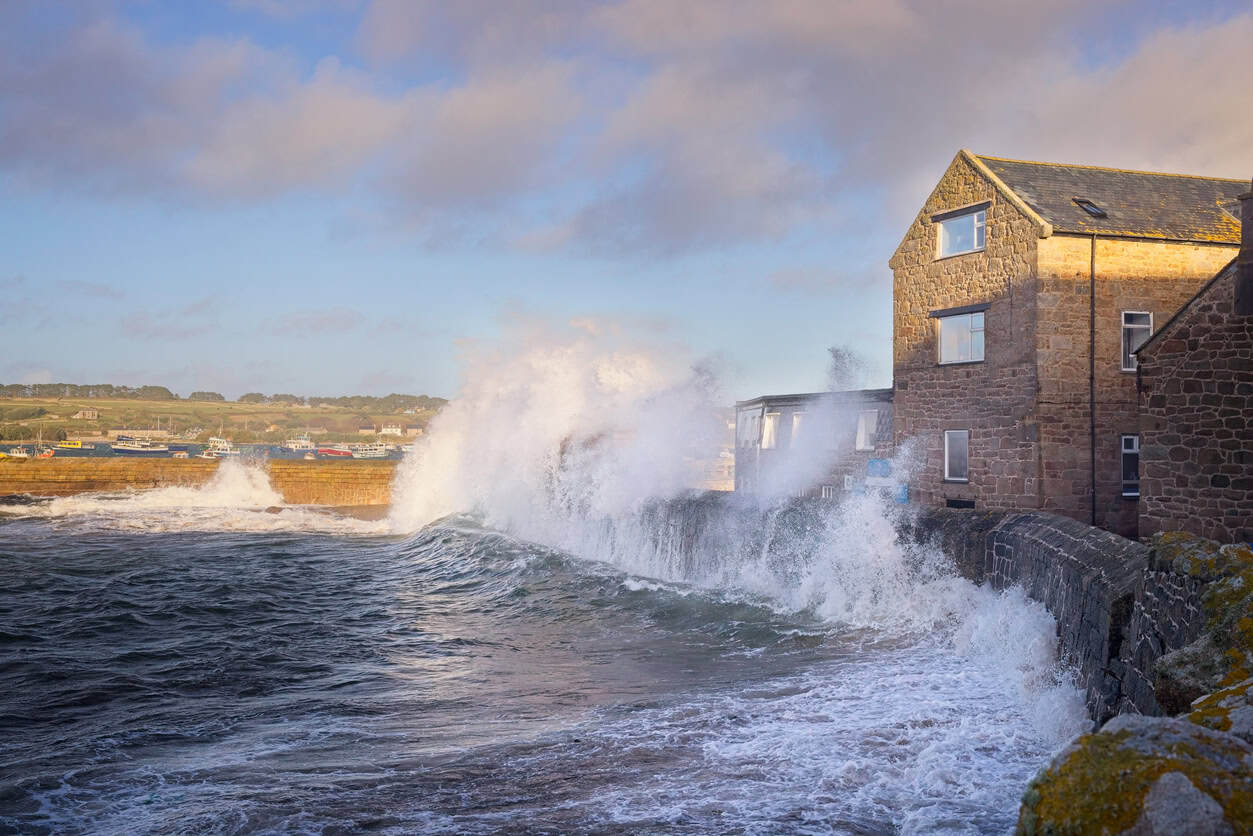 Waves overtopping a harbour wall on the Isles of Scilly, the wave action that rides on top of a storm surge.