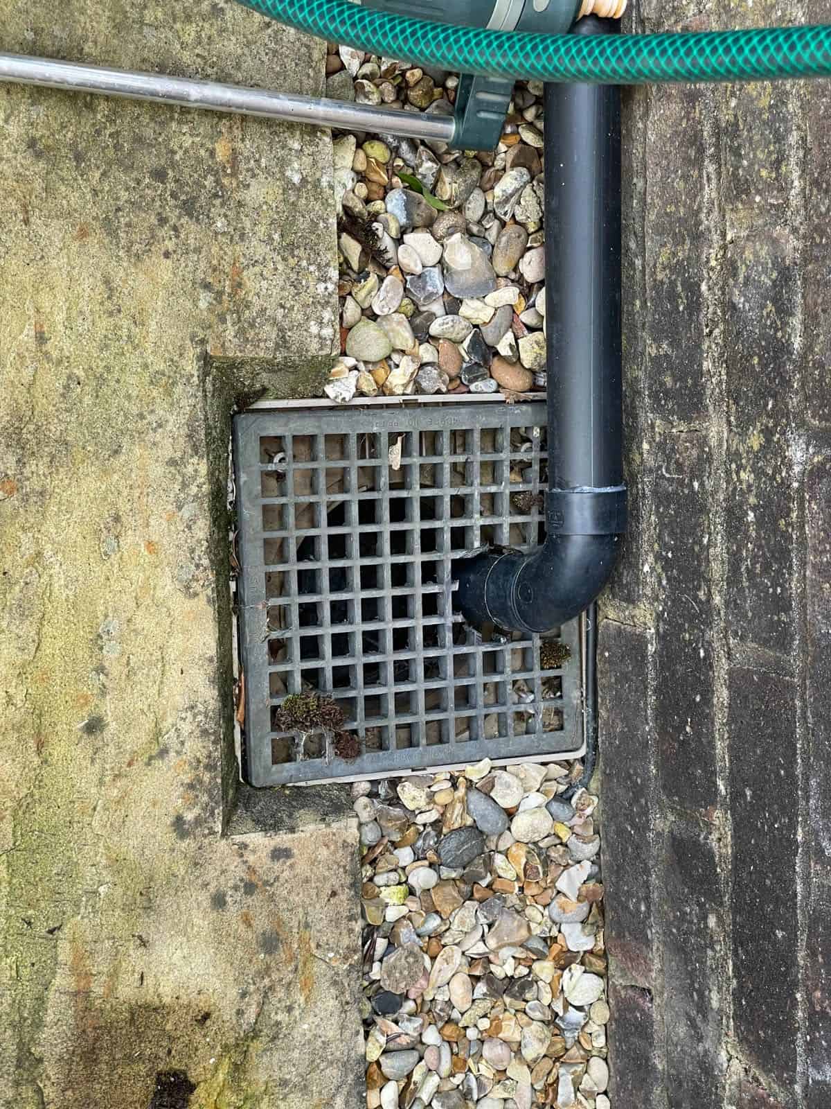 Rainwater downpipe discharging to a gully grating beside a house, a surface water drain rather than a culvert.